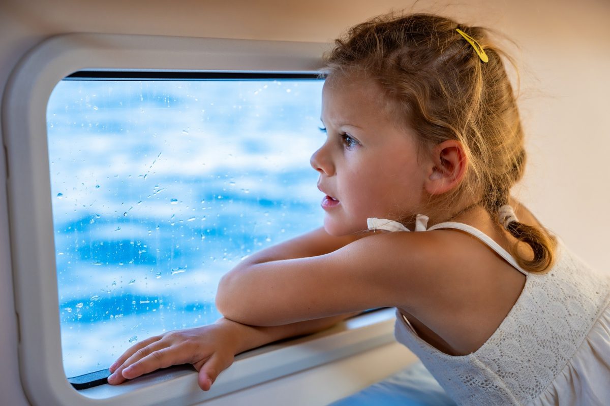 Blond little girl sits in the cabin of a yacht and looks out the window during a sea crossing. Yacht
