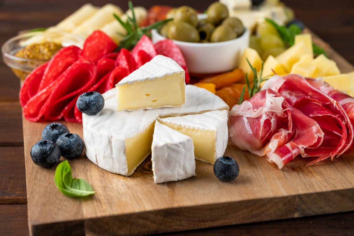 Charcuterie board with a variety of cheeses, salami, chorizzo, prosciutto, nuts, bread, berries