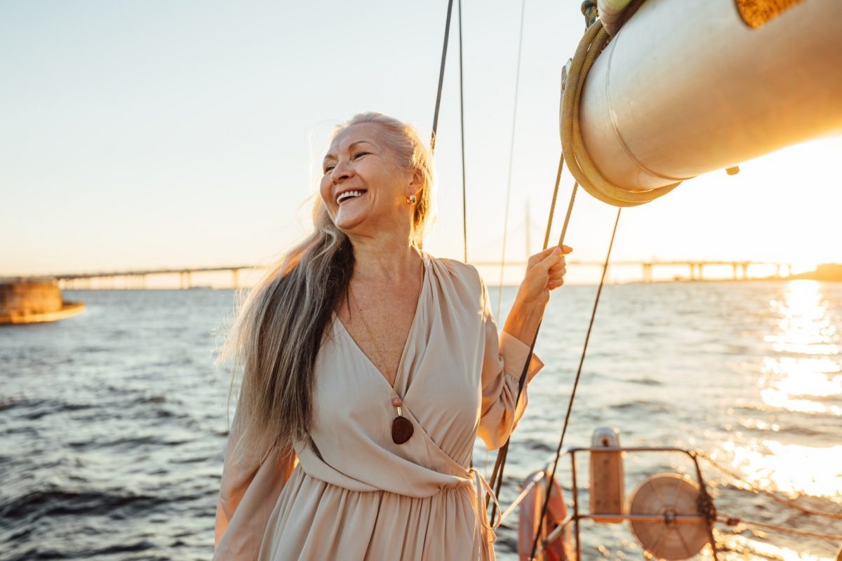 Happy mature woman standing on a yacht at sunset and looking away