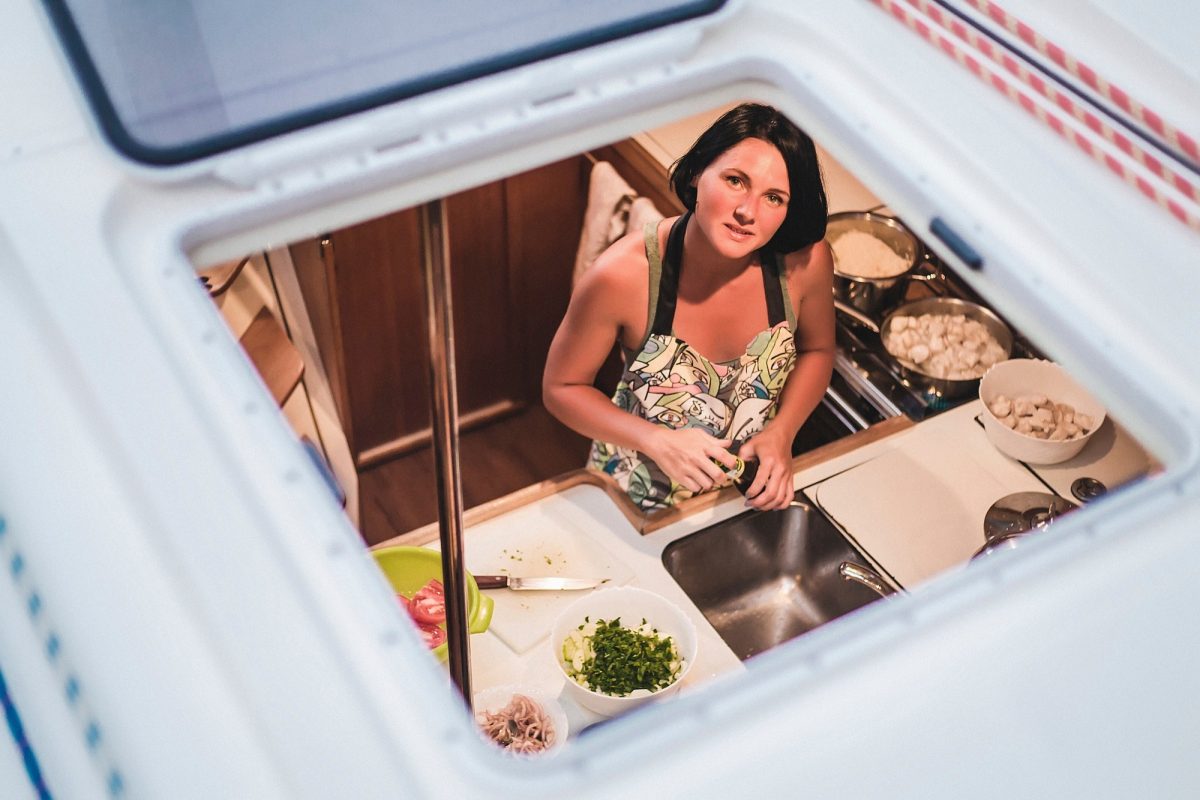 Portrait of young woman through yacht hatch preparing food in kitchen, Croatia