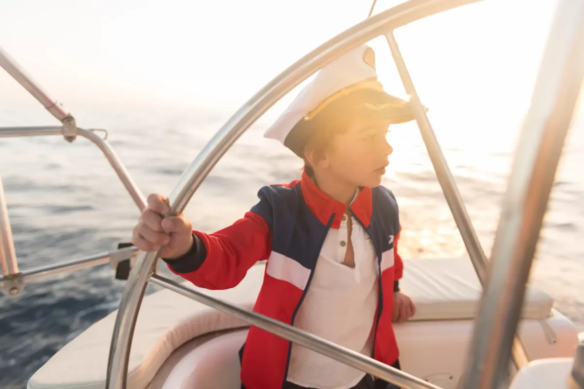 Smiling girl holding steering wheel on yacht on water