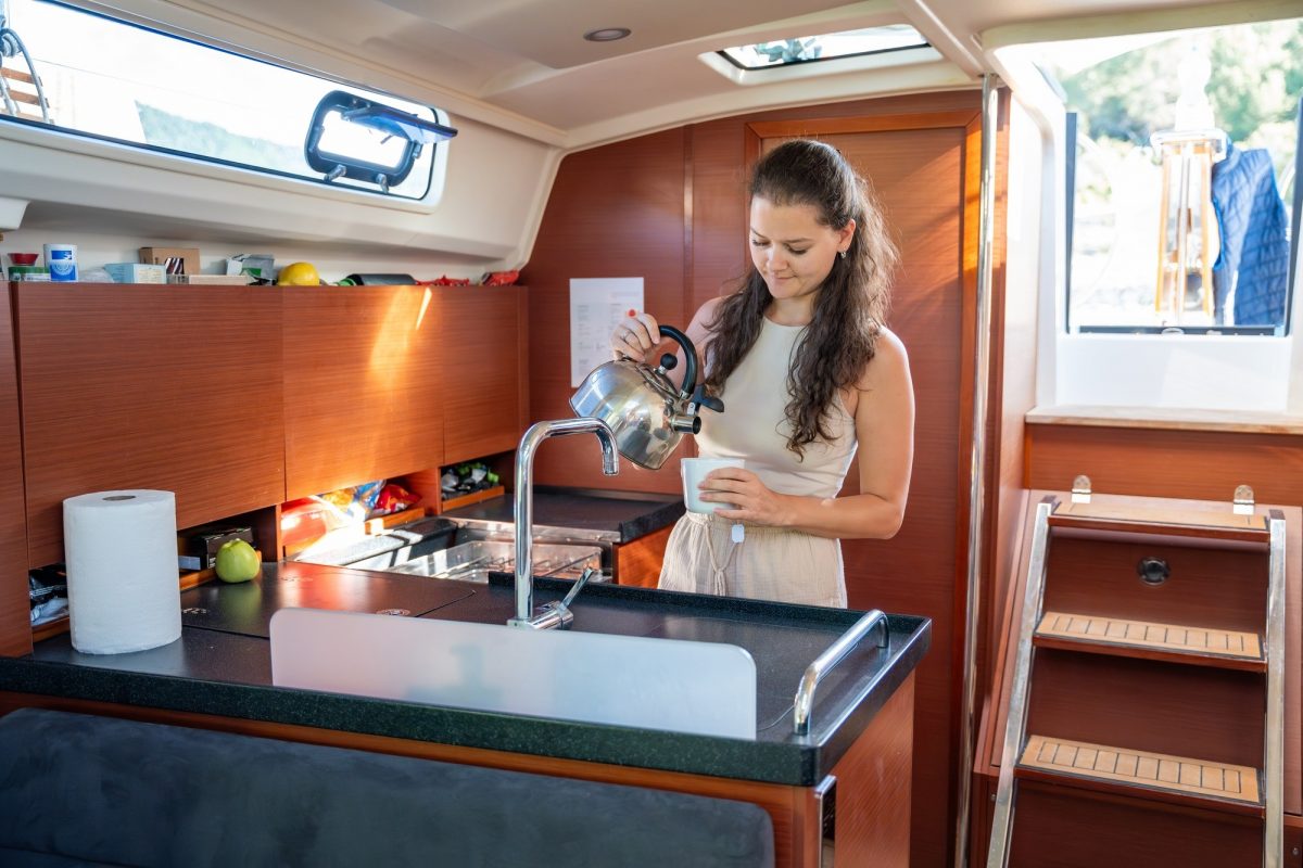 Young woman standing and preparing tea in kitchen in cabin of modern yacht during sailing in sea